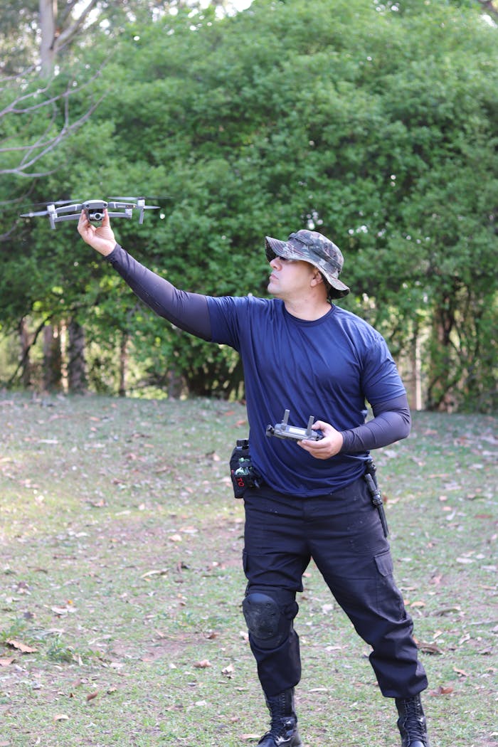 A man in tactical gear controls a flying drone outdoors, showcasing modern technology in action.